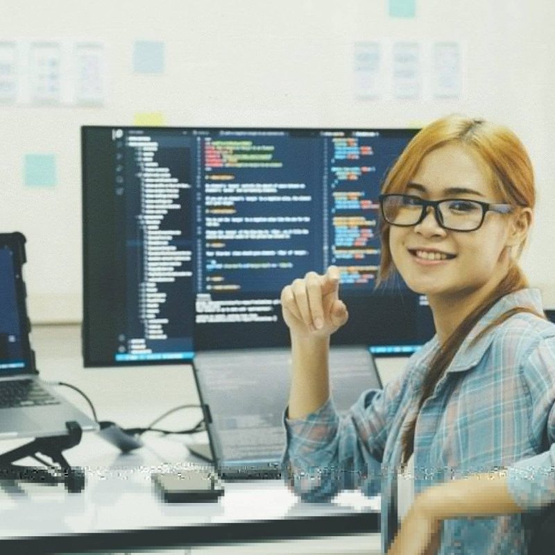Young programmer or IT specialist satisfied with her work done. Happy young woman working on laptop while sitting at her working place in office.